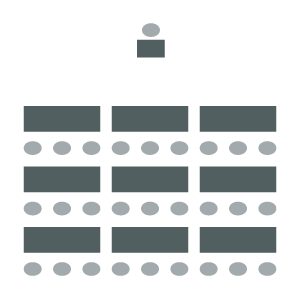 Room arranged with rectangular tables in rows with chairs on one side facing podium at front of room.