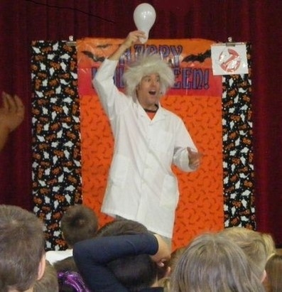 Man in a lab coat and white wig holding a lightbulb over his head